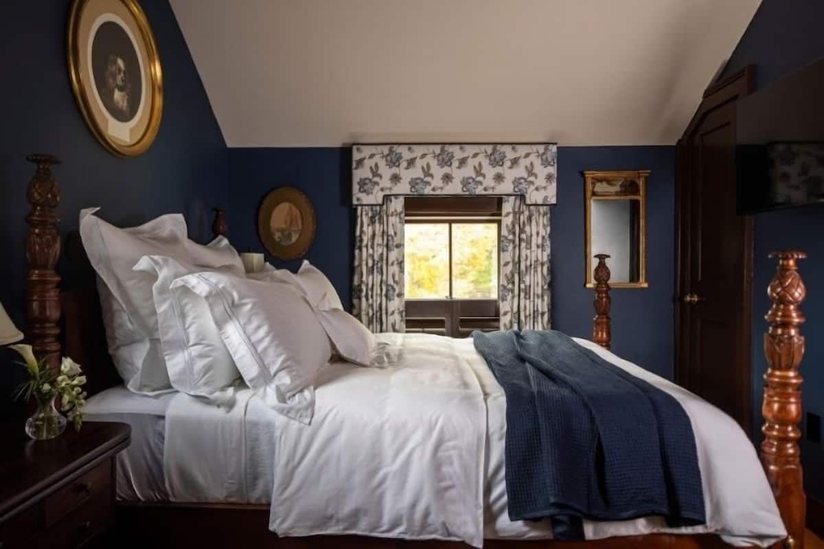 A bedroom with a large bed, a dresser, a mirror, and a window with floral curtains.