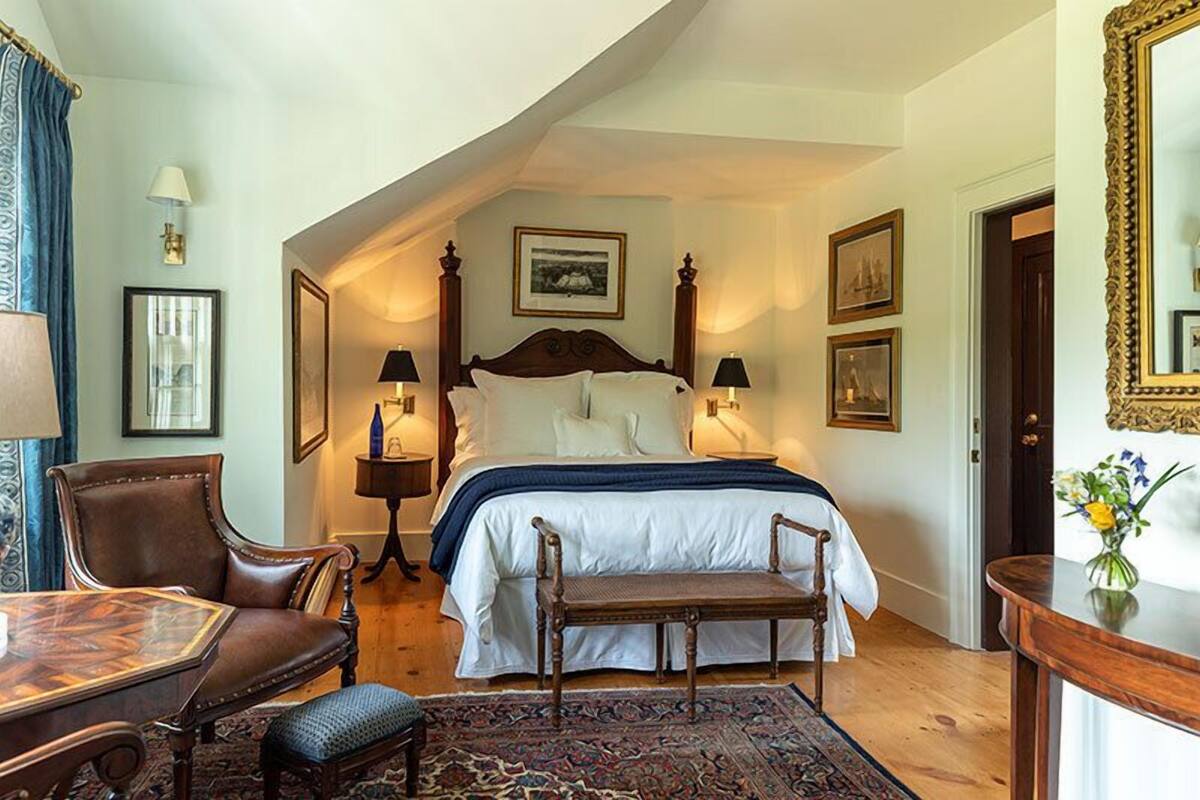 A bedroom with a large bed, two bedside tables with lamps, a chair, a small table, and a mirror.