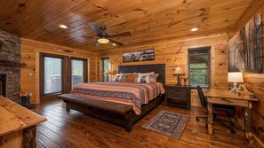 Une chambre dans un chalet en rondins, avec un plafond en bois, un lit recouvert d’une literie à motifs, un bureau avec une lampe et un tableau accroché au mur.