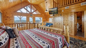 A log cabin room with a large bed, a television, and a view of the mountains. - Feel Like A Millionaire Relaxing In These Views (SEVIERVILLE)