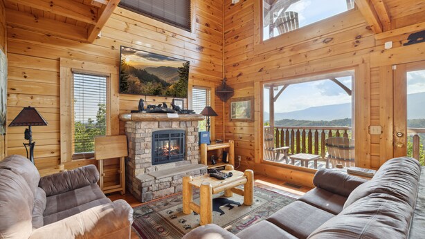 A cozy log cabin interior with a fireplace, wooden furniture, and a scenic view through large windows. - Feel Like A Millionaire Relaxing In These Views (SEVIERVILLE)