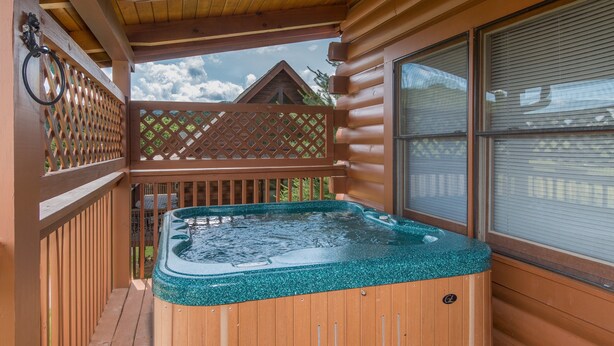 A wooden deck with a hot tub, wooden railings, and a view of a house in the background.