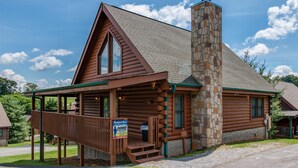 A log cabin with a stone chimney, a porch, and a sign advertising a 1922 trout fishing event.