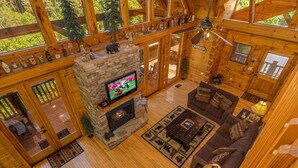L’intérieur d’un chalet confortable, avec une cheminée en pierre, des meubles en bois et un téléviseur.