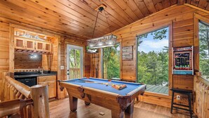 A wooden cabin with a pool table, wooden cabinets, and a large window overlooking a forest. - Come getaway to a cabin in the Moonlit Pines (SEVIERVILLE)