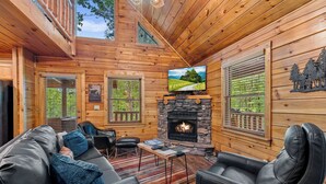 A cozy log cabin interior with a stone fireplace, leather furniture, and a television mounted above it. - Come getaway to a cabin in the Moonlit Pines (SEVIERVILLE)