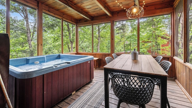 A wooden deck with a hot tub, a table, and chairs, surrounded by large windows offering a view of trees. - Come getaway to a cabin in the Moonlit Pines (SEVIERVILLE)
