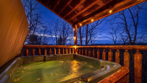 A hot tub with a wooden deck and railing, surrounded by trees. - Making Memories You'll Never Forget (SEVIERVILLE)