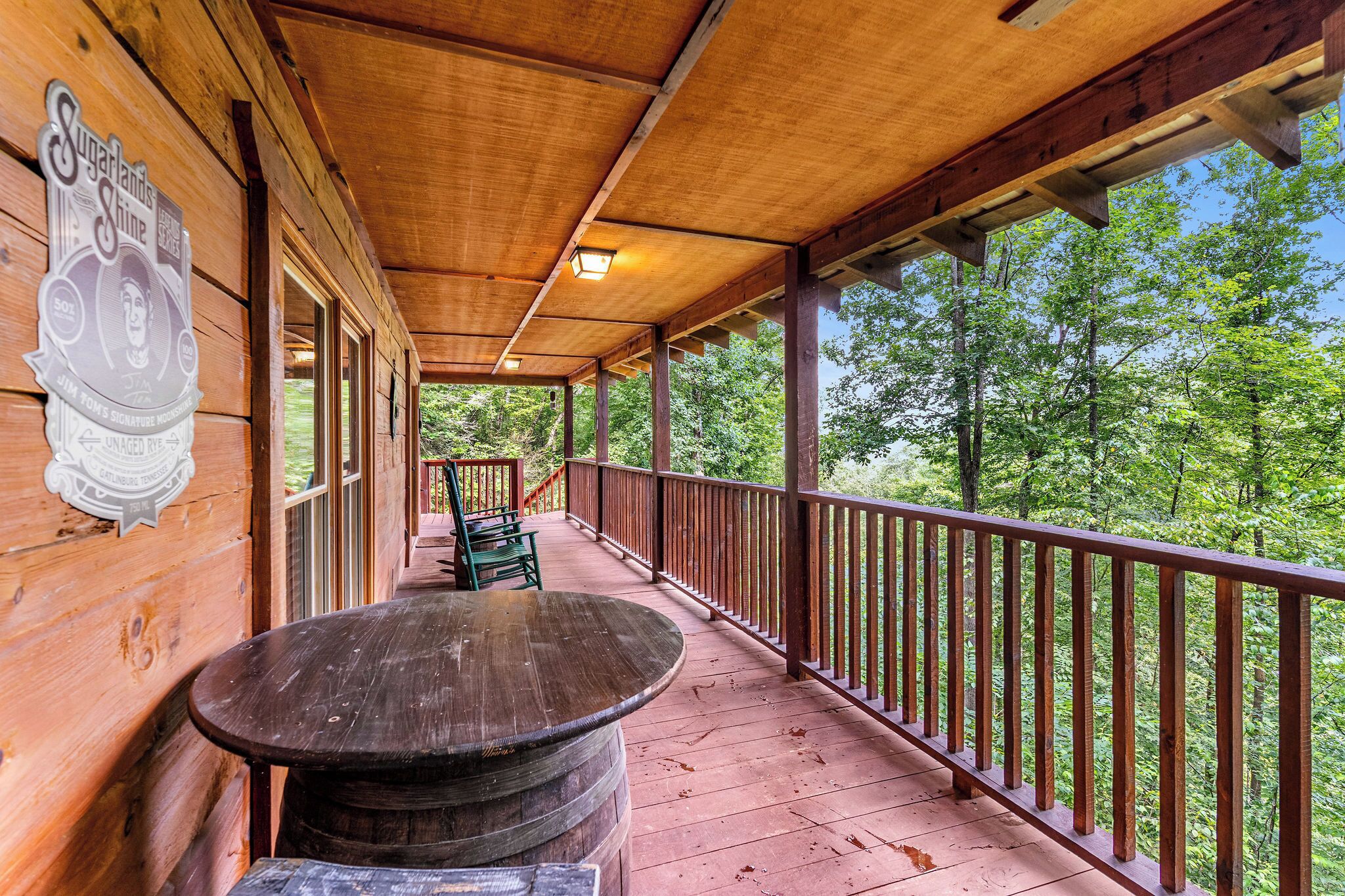 A wooden deck with a table and chairs, surrounded by a railing, overlooking a forested area.