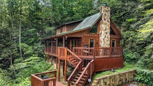Une cabane dotée d’une cheminée en pierre, d’une terrasse en bois et d’un escalier menant à l’entrée.
