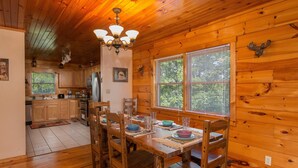 L’intérieur d’un chalet en bois, avec une table à manger dressée pour quatre personnes, un plancher en bois et un coin cuisine visible au fond.