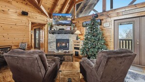 Un acogedor interior de cabaña con chimenea, televisor y un árbol de Navidad.