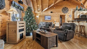 Interior acogedor de una cabaña de troncos con una mesa de comedor de madera, un sofá cómodo, un árbol de Navidad y una zona de cocina.