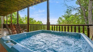 Un jacuzzi en una terraza de madera con vista a árboles y montañas.