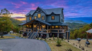 Une grande maison à étages, dotée d’un porche avant imposant, de détails en pierre et offrant une vue pittoresque sur les montagnes.