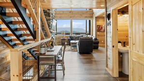 Un intérieur en bois avec un escalier, un coin repas, un canapé et une vue sur l’extérieur.
