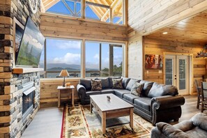 A cozy living room with a stone fireplace, a leather sofa, and large windows offering a scenic view. - Wow Yourself With Luxury Beyond Belief at Morning Wood (SEVIERVILLE)