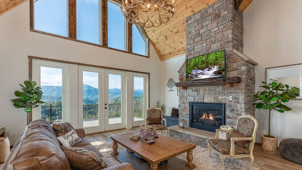A spacious living room with a stone fireplace, leather sofa, and large windows offering mountain views.
