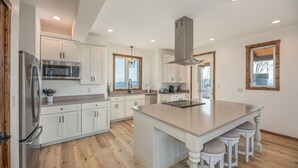 A modern kitchen with white cabinetry, a stainless steel refrigerator, a microwave, and a large island with bar stools.