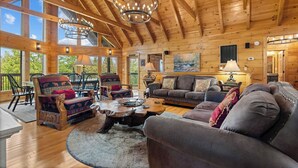 Un interior de cabaña de madera espacioso, con techo alto, ventanas amplias y una zona de estar acogedora con chimenea.
