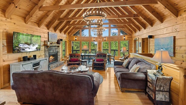 Interior espacioso de una cabaña de madera con chimenea, asientos cómodos y ventanas amplias que ofrecen vistas del exterior.