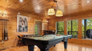 Un interior de madera con mesa de billar, un cuadro de un oso y ventanas amplias.