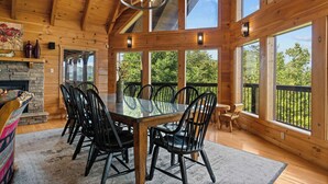 Un interior de madera con una gran mesa de comedor, sillas negras y una chimenea de piedra.