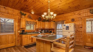 A wooden cabin interior with a central island, wooden cabinets, a chandelier, and a refrigerator.