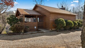 A wooden cabin with a sloped roof, a covered porch, and a gravel driveway.