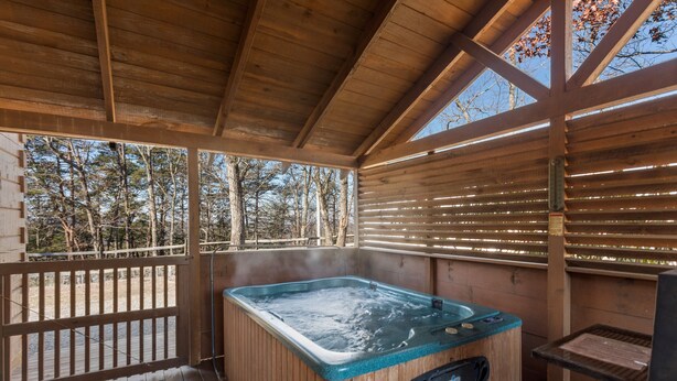 A wooden hot tub in a covered outdoor area with a wooden deck and a view of trees.