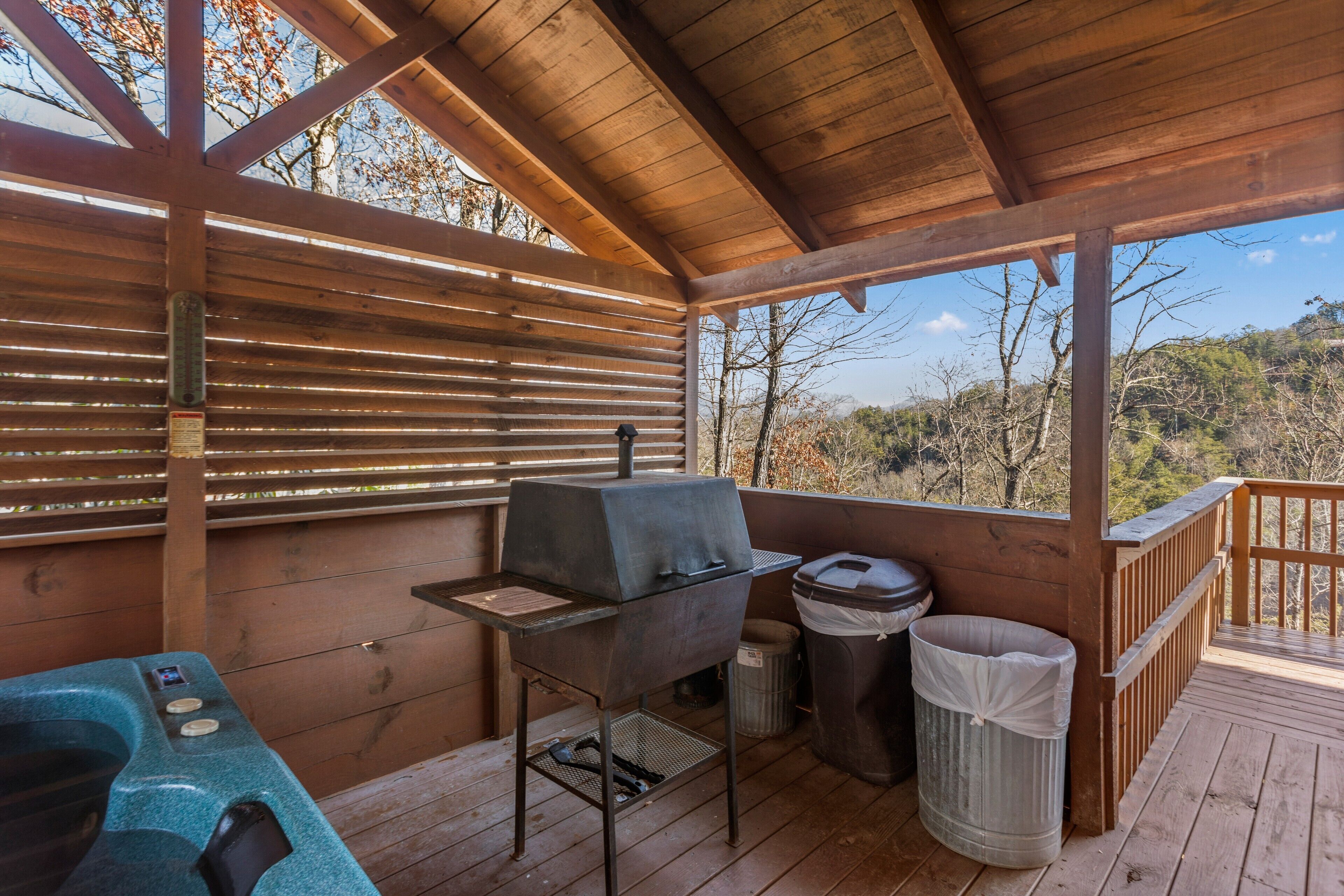 Un espacio al aire libre techado con una parrilla, un jacuzzi y un bote de basura.