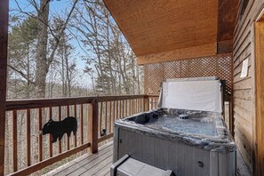 Une terrasse en bois avec un jacuzzi, une clôture en bois et une décoration représentant la silhouette d’un ours.