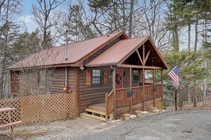 Eine rustikale Holzhütte mit Veranda und kleiner Terrasse, mit einer amerikanischen Flagge.