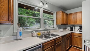 A kitchen with wooden cabinets, a double sink, and a window with a view of greenery. - Mountain Views-Hot Tub-Fireplace-Close to Dollywood (SEVIERVILLE)