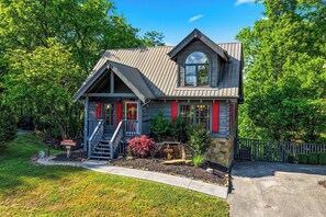 A two-story house with a front porch, a stone foundation, and a fenced yard. - A Breath Of Fresh Air No Matter The Weather (PIGEON FORGE)