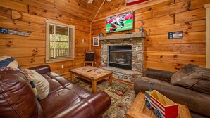 A wooden cabin interior with a stone fireplace, leather sofas, a television, and an American flag. - Freedom Rings Where Mountains Sing (SEVIERVILLE)