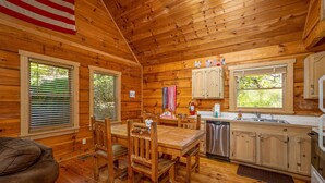 A wooden cabin interior with a dining table, chairs, a kitchen area, and an American flag. - Freedom Rings Where Mountains Sing (SEVIERVILLE)