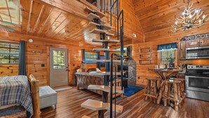 A log cabin interior with a spiral staircase, a bed, a sofa, a kitchen area, and a dining table. - Smoky Mountain Treehouse with hot tub and dog-friendly (GATLINBURG)