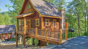 A wooden cabin with a balcony, surrounded by trees. - Smoky Mountain Treehouse with hot tub and dog-friendly (GATLINBURG)