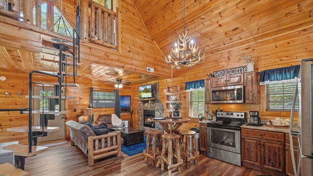 A cabin interior with a wooden interior, a stone fireplace, a kitchen area, and a living room with a sofa and a coffee table. - Smoky Mountain Treehouse with hot tub and dog-friendly (GATLINBURG)
