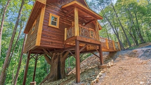 A wooden cabin with a balcony, built on stilts above a tree, surrounded by a forest. - Smoky Mountain Treehouse with hot tub and dog-friendly (GATLINBURG)