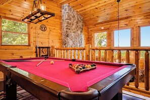 A pool table with a red felt surface, surrounded by wooden walls and a stone feature.