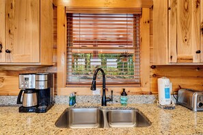 A kitchen with wooden cabinets, a stainless steel sink, a coffee maker, and a toaster. - Surrounded By Mountain Beauty (GATLINBURG)