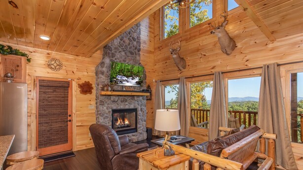 A cozy log cabin interior with a fireplace, leather seating, and a scenic view.