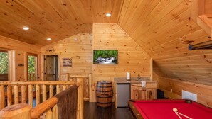 A wooden cabin interior with a pool table, a bar, and a small kitchen area.