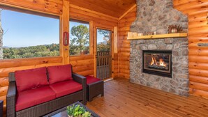 A log cabin with a stone fireplace, a red sofa, and a view of the forest.