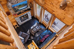 A cabin interior with a stone fireplace, a sofa, a television, and a deer head decoration. - Surrounded By Mountain Beauty (GATLINBURG)