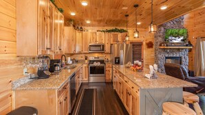 A wooden cabin interior with a kitchen featuring granite countertops, stainless steel appliances, and a stone fireplace.