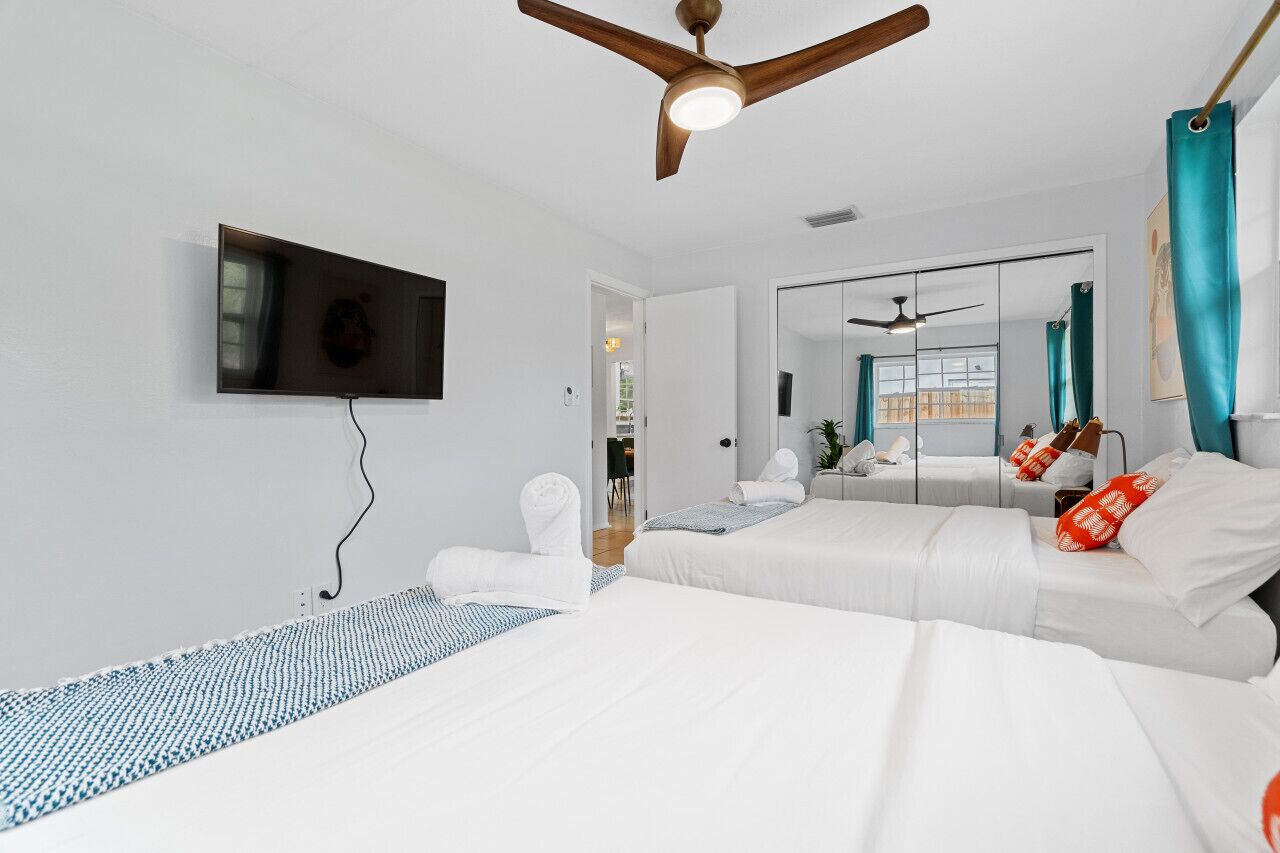 A modern hotel room with a large bed, a ceiling fan, a flat-screen TV, and a bathroom mirror.