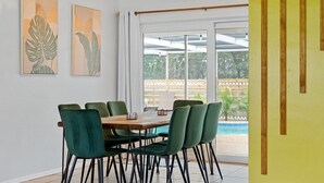 A dining area with a table and chairs, artwork on the wall, and a view of a pool through large windows. - Boho Heated Pool House w/Gym <20min to Beaches! (Largo)